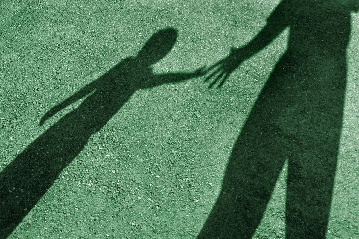 A silhouette of an adult holding hands with a child, symbolizing protection and care on synthetic grass.